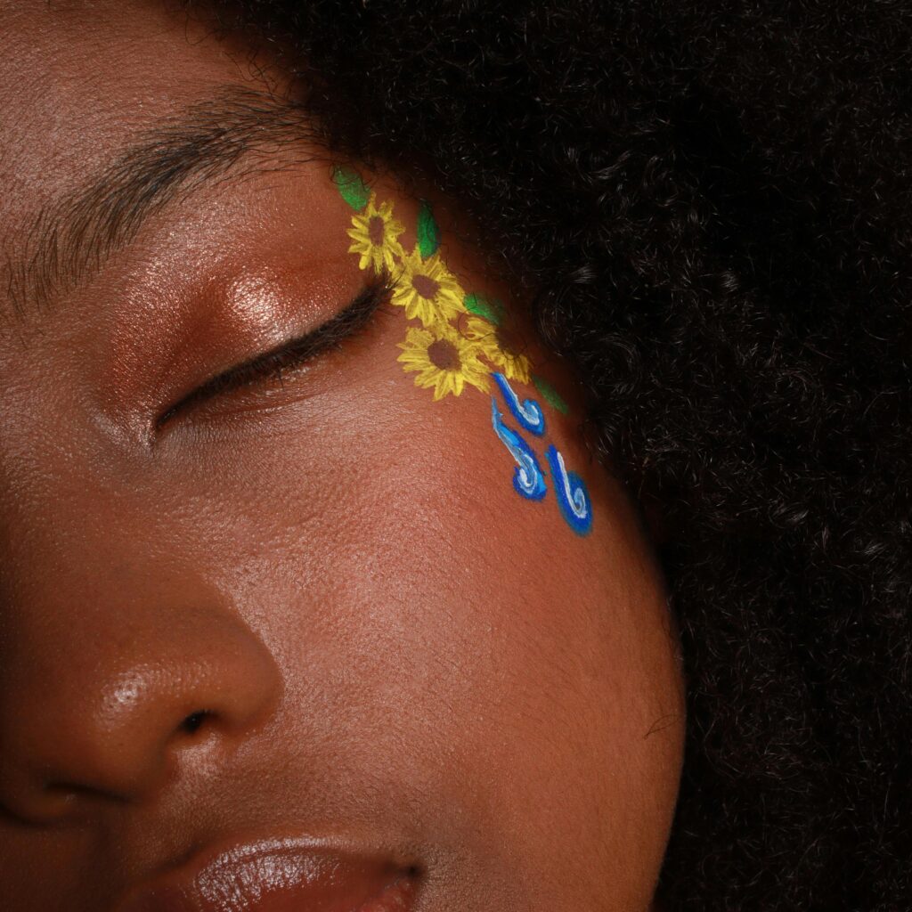 Close-up portrait of a woman with floral and artistic face paint, eyes closed.